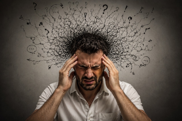 Hombre con gesto de angustia y confusión mental rodeado de pensamientos caóticos que representan la rumiación mental.